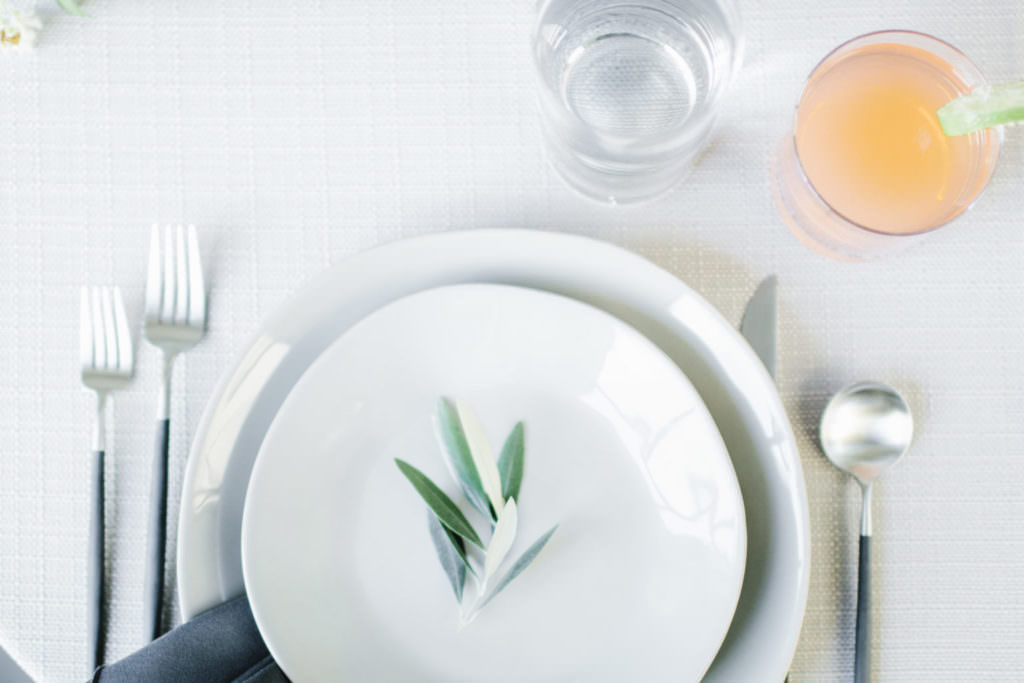 Table setting with white plates and a sprig of a herb, glass of water, silver cutlery