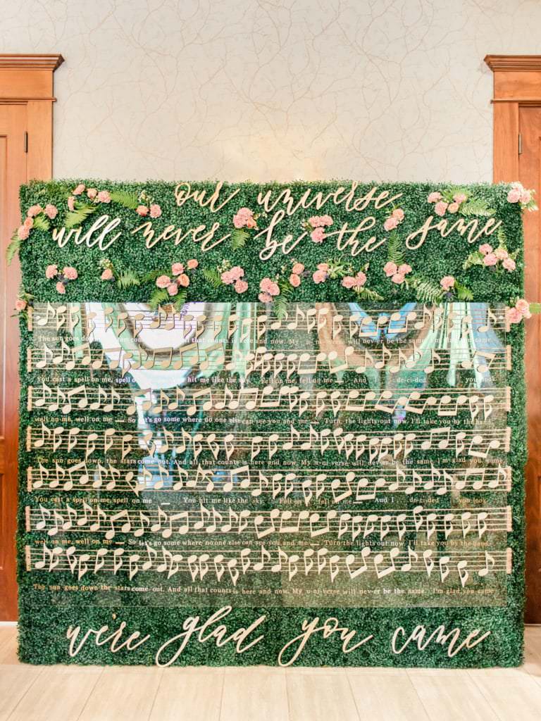 Song lyrics displayed on a clear board with musical notes and green foliage and flowers behind.