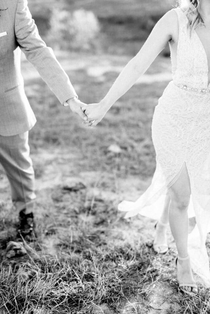 Black and white image of bride and groom walking whilst holding hands