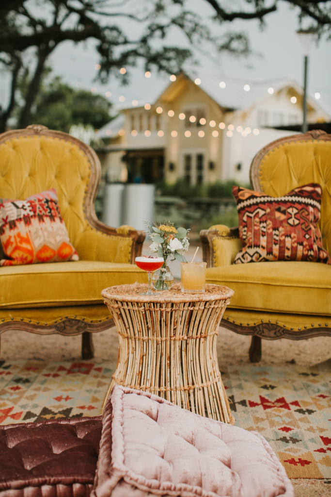 2 mustard colored chairs with cushions and cocktails sitting on a wicker style table