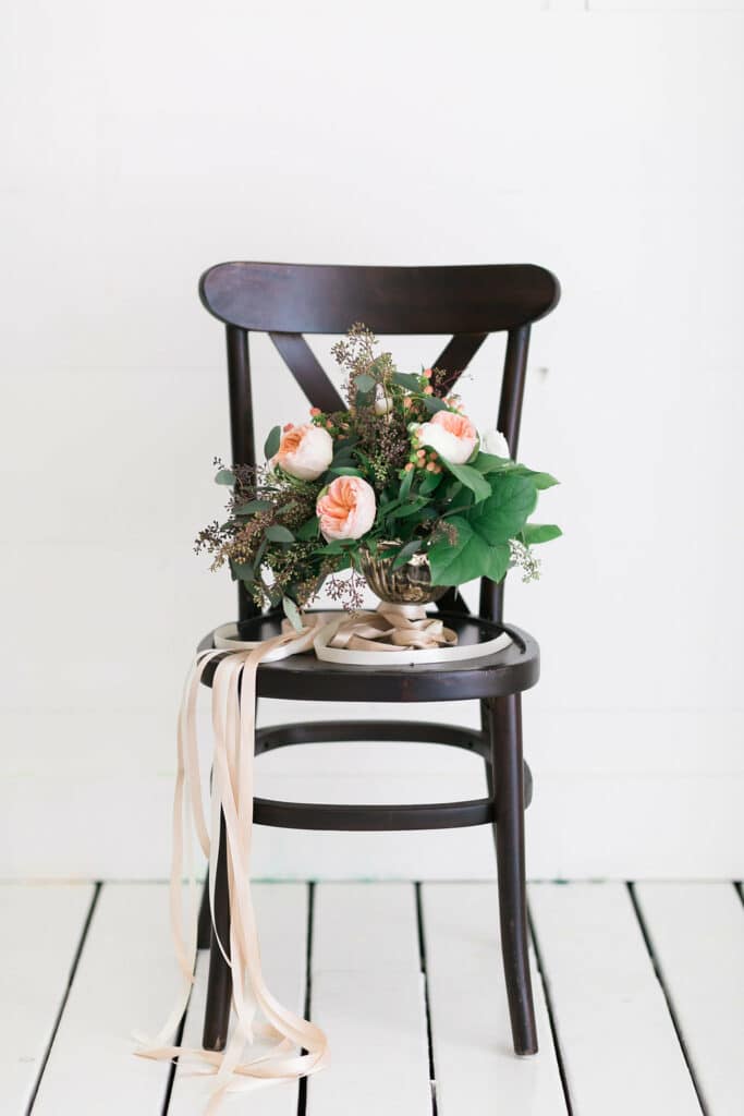 Brown chair with a bouquet of green and pink flowers with a beige satin ribbon