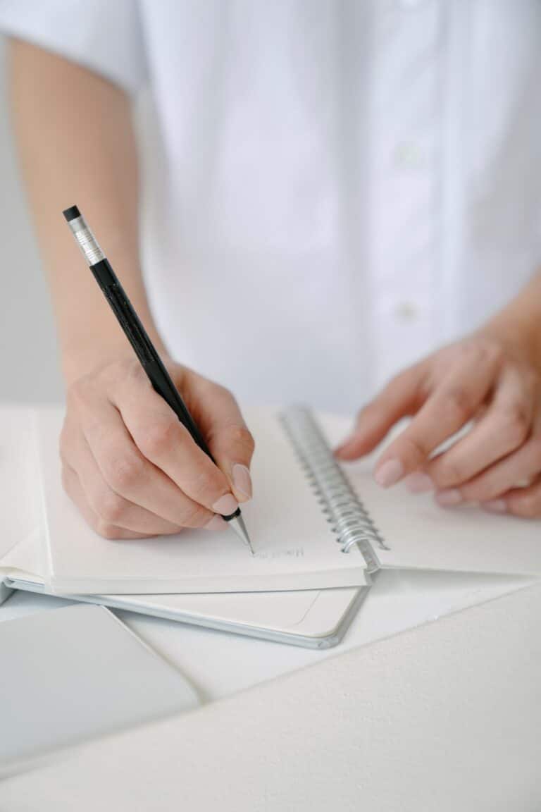Women writing on a note pad with a black pen. The ultimate guide to blogging for wedding pros.