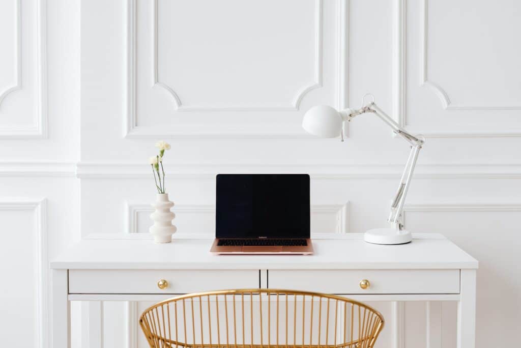 Desk with laptop, lamp and gold chair against white ornate wall