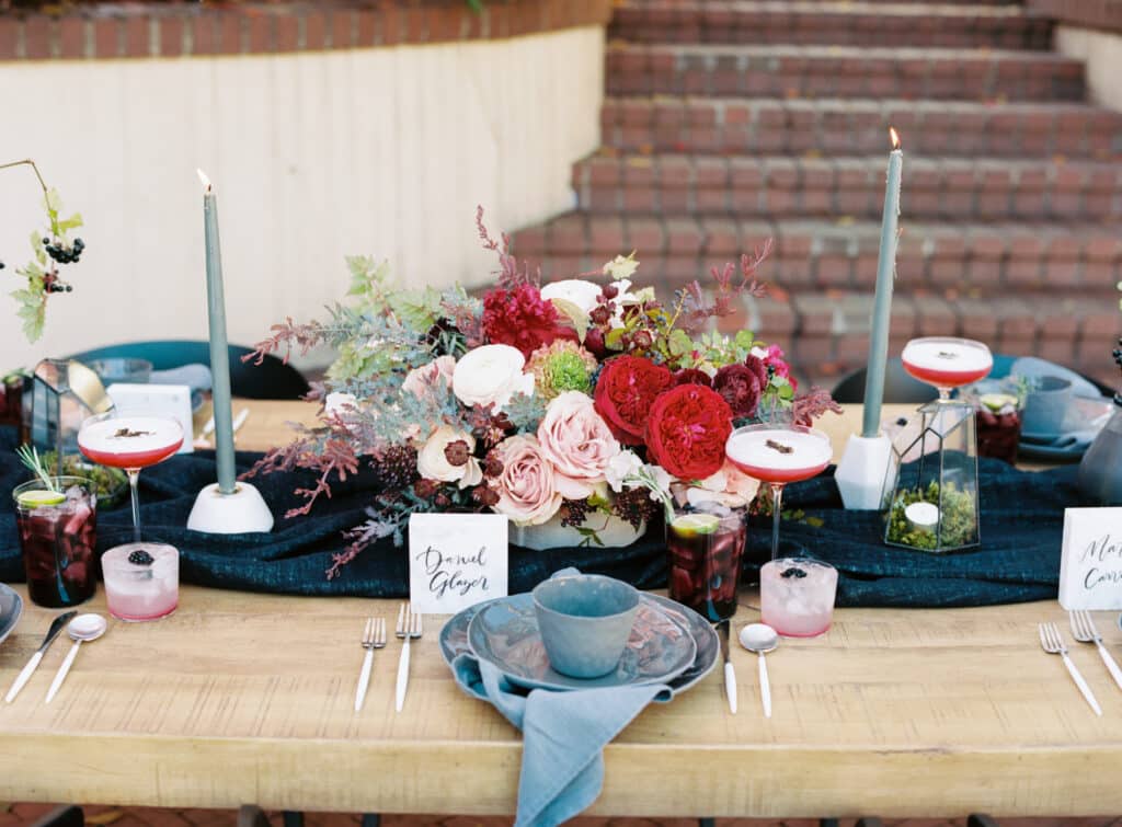 wedding table with colorful red blooms, blue plates, pink cocktails and silverware