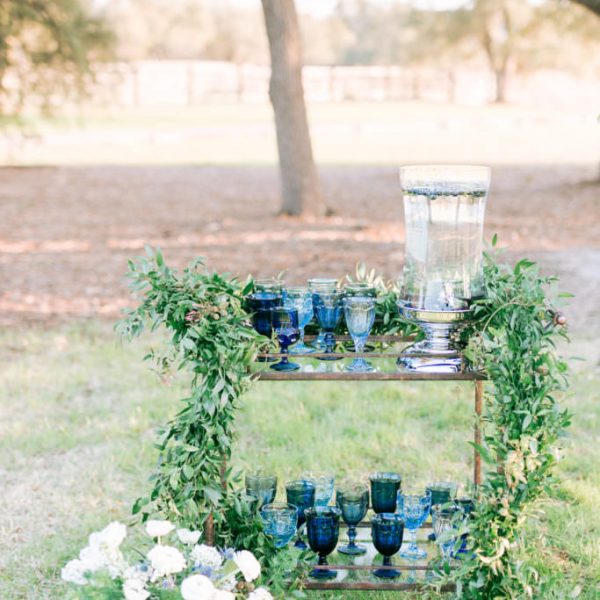 Wedding water station with pitcher and blue glasses on a stand with green foliage